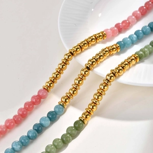 Detail of colorful stone and gold bead bracelets on white ceramic plate, bohemian style