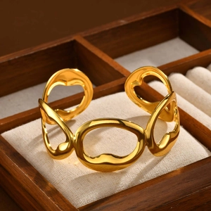 Detailed view of golden open cuff bangle with hollow wavy geometric links on linen cushion