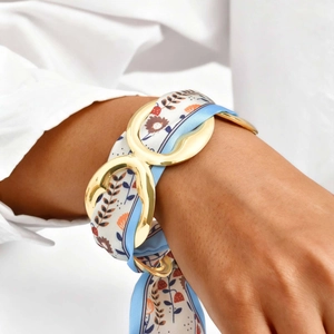 Close-up of golden geometric metal clasp with blue floral silk scarf wrap bracelet