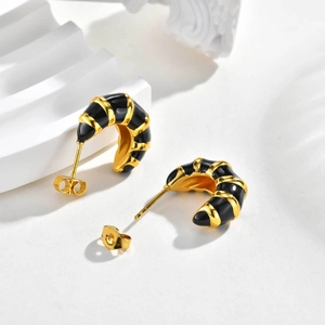 Détail de boucles d'oreilles en C plaqué or avec rayures en émail noir et fermoirs papillon
