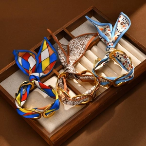 Three-piece gold stainless steel cuff bracelet set with assorted silk scarves on a wood tray