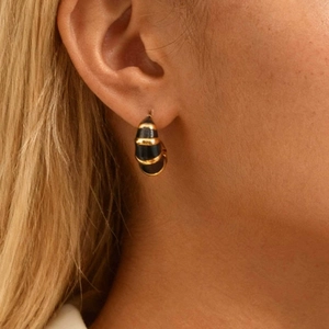 Boucles d'oreilles C dorées avec rayures en émail noir portées par une femme mannequin