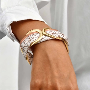 Detail of gold geometric hollow cuff bracelet with silk scarf insert on woman's wrist