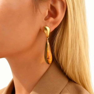 Golden teardrop stainless steel earrings with amber resin pendant worn by a model
