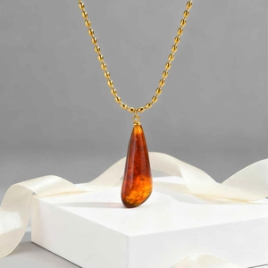 Golden teardrop resin pendant necklace with polished amber finish on a beaded chain