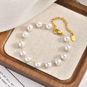 Elegant gold finish stainless steel bracelet with white pearls on a minimalist wooden tray