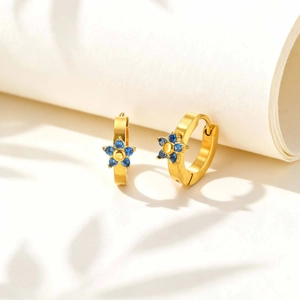 Dettaglio di orecchini a cerchio dorati con fiori in zircone blu su sfondo bianco