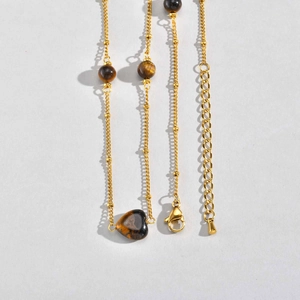 Détail du collier doré avec pierre œil de tigre en cœur et petites perles d'or