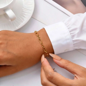 Close-up of a gold Figaro link bracelet worn on a wrist with an elegant white shirt cuff