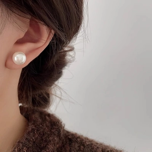 Elegantes pendientes de perlas redondas con brillo premium lucidos por una modelo
