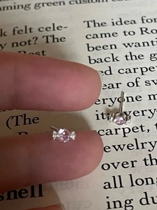Detailed view of mini candy-shaped pink zircon stud earrings held by hand for size scale