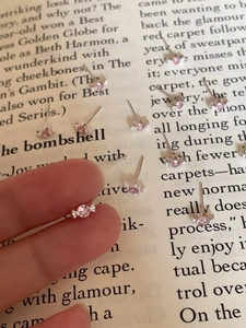 Close-up of a mini silver stud earring with pink zircon held by hand over a vintage book