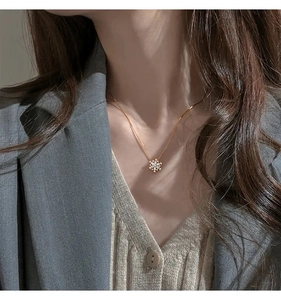 Dettaglio collana con ciondolo a fiocco di neve rotante argento su maglione beige