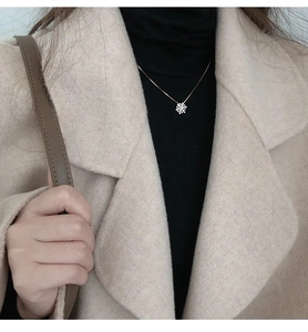 Collana con ciondolo a fiocco di neve argento indossata su cappotto cammello