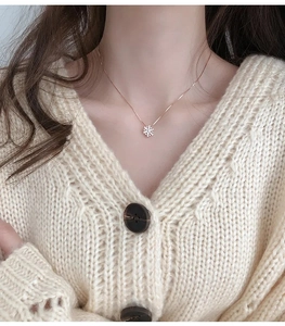 Dettaglio della collana con fiocco di neve in oro rosa indossata su un maglione lavorato
