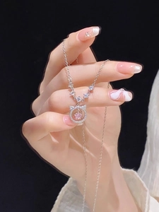 Close-up of S925 silver cat necklace with pink gemstone held in hand on black background