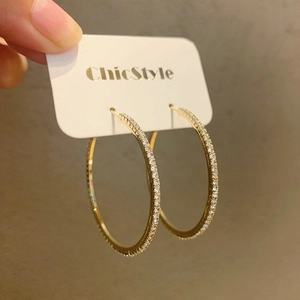 Makroaufnahme großer goldener Creolen mit funkelnden Zirkonsteinen im Pavé-Stil