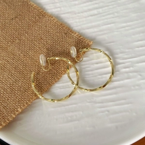Detalle de pendientes de aro dorados trenzados con clips y almohadillas de silicona