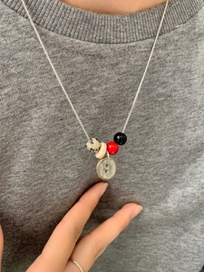 Detail van kralenketting met gevlekte steen en knoop hanger op een grijze trui