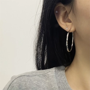 Primer plano de una modelo con aretes de aro grandes plateados con diseño trenzado pulido