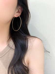 Close-up of model wearing minimalist large gold hoop earrings with woven texture