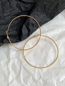 Macro detail of large gold hoop earrings featuring a fine knurled metallic texture