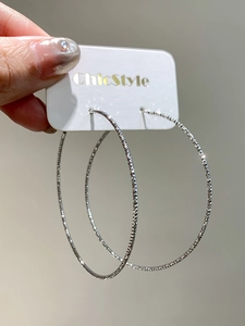 Close-up of large silver hoop earrings with a textured shimmering finish on display