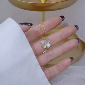 Close-up of golden four-leaf clover necklace with opal petals worn on neck