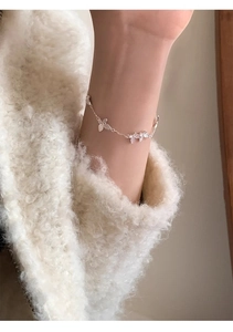 Detail of silver butterfly bracelet on model wearing a soft white fleece jacket