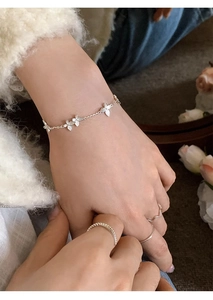 Detailed view of dainty S925 silver butterfly bracelet and stacked rings on model