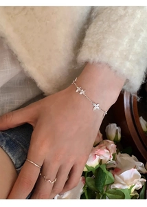 Close-up of silver butterfly clover bracelet on wrist with elegant minimalist rings