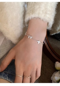 Close-up of a silver floral charm bracelet on a wrist with soft lighting and cozy apparel