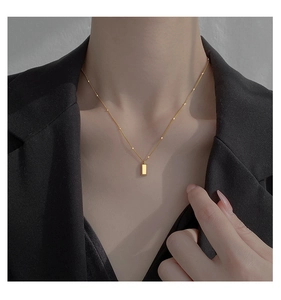 Close-up of minimalist gold bar necklace on satellite chain worn by model in suit
