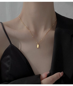 Close-up of minimalist gold bar pendant on a thin bead chain necklace worn by a model
