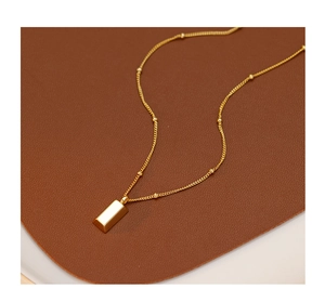 Detail of gold bar pendant necklace with small beads on a brown leather surface