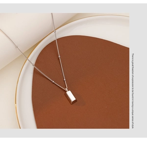 Detailed close-up of a silver rectangular bar pendant on a delicate beaded ball chain