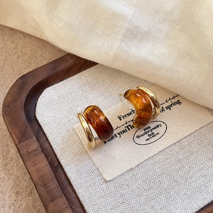 Detalle de pendientes C dorados vintage con resina de ámbar en tarjeta beige
