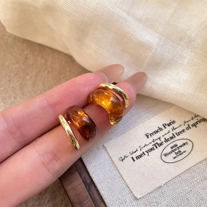 Primer plano de pendientes dorados vintage con resina de ámbar texturizada y metal pulido