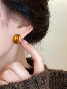 Detalle de pendientes de resina ámbar y metal dorado con un jersey de punto grueso