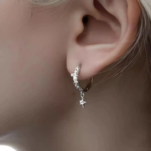 Primer plano de pendientes de aro plateados con estrella y circonitas en el modelo