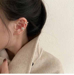 Primer plano de pendientes ear cuff de plata con mariposa, flor y circonitas