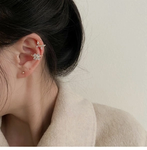 Primer plano de ear cuffs de mariposa y flores doradas con circón en la oreja del modelo