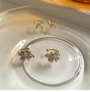 Vista macro de pendientes de clip de flores de circonita y mariposas en plato de cristal