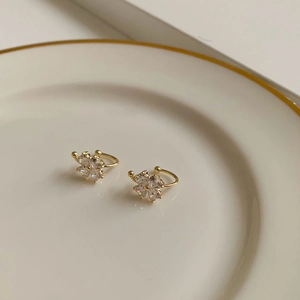 Detalle de pendientes de clip trébol dorado con circonitas en forma de corazón brillante