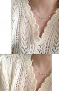 Close-up of a silver rice bead chain necklace layered over a white crochet sweater