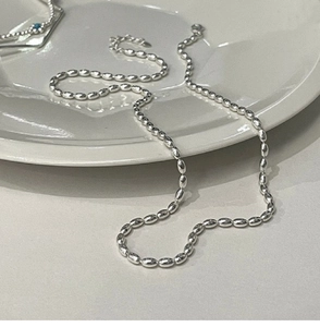 Detail of silver oval bead necklace with lobster clasp on a white ceramic tray