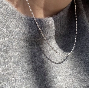 Macro shot of silver-plated oval bead chain necklace on a grey knitted sweater