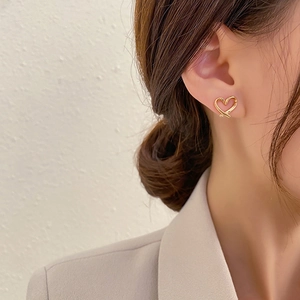 Close-up of gold hollow heart-shaped clip-on earring worn by model in gray blazer