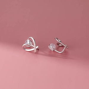 Minimalist silver heart-shaped ear clips with comfortable clear silicone pads on pink backdrop