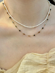 Dettaglio della collana girocollo dorata con perline colorate e perle bianche sul collo